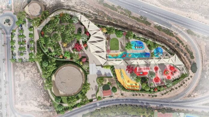 Aerial view of a hillside park with a circular plaza, green spaces, and colorful playground areas against a road-lined perimeter for context.