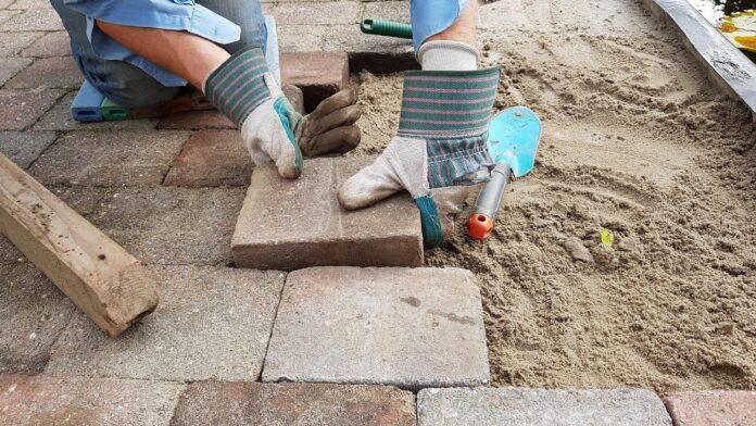 Worker wearing gloves places a brick on a paved area at a construction site.