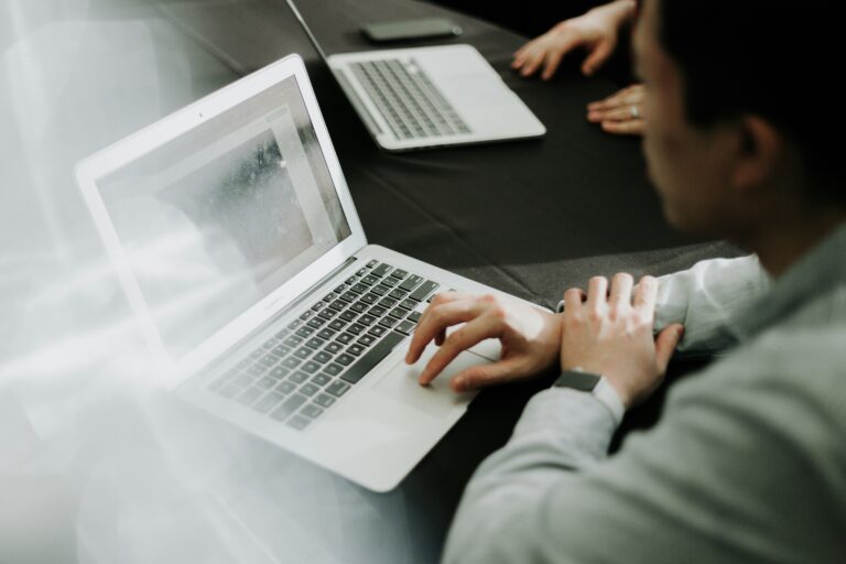 Two people typing on silver laptops at a dark table during a collaborative work session.