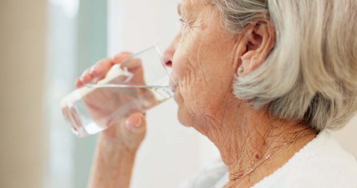 Older woman drinks water from a glass, shown in profile.
