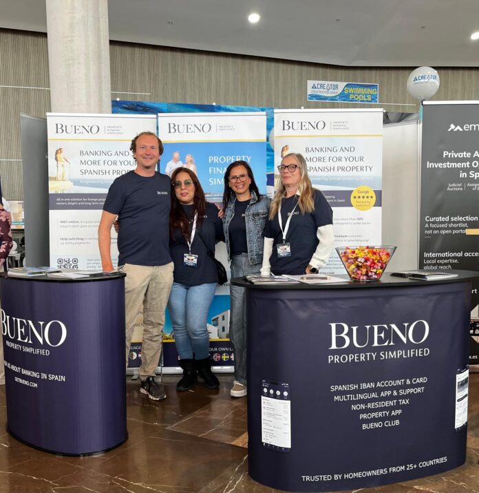 Group of four people standing behind Bueno booths at a trade show, smiling for the camera with banners reading 'BUENO Property Simplified' behind them.