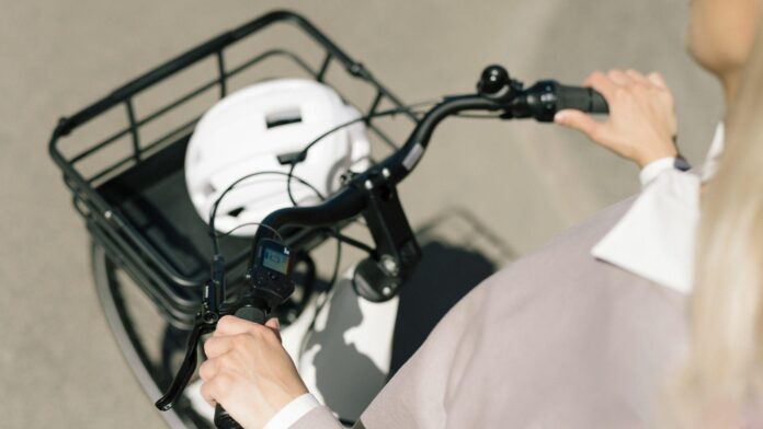 Person riding a bicycle seen from above, hands gripping handlebars, white helmet in the front basket