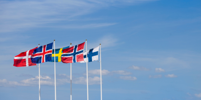 Row of Nordic country flags (Denmark, Iceland, Sweden, Norway, Finland) waving on flagpoles against a clear blue sky