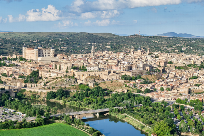 Aerial view of Toledo, Spain: the Tagus River curves through the city with medieval walls and terracotta rooftops on rolling hills.