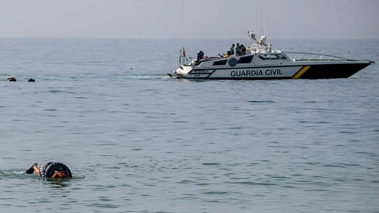 Coast guard patrol boat labeled Guardia Civil on the sea with a swimmer nearby in the foreground.","A Guardia Civil rescue vessel on calm water as a swimmer with a flotation ring is close by.","Rescue boat at sea watches over a swimmer near a black flotation ring in the foreground.